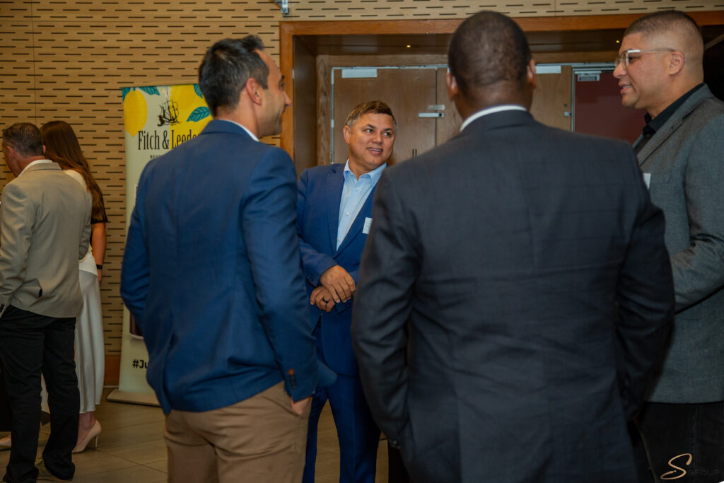 Group of business professionals conversing at an indoor networking event, with a lemon-themed banner in the background.