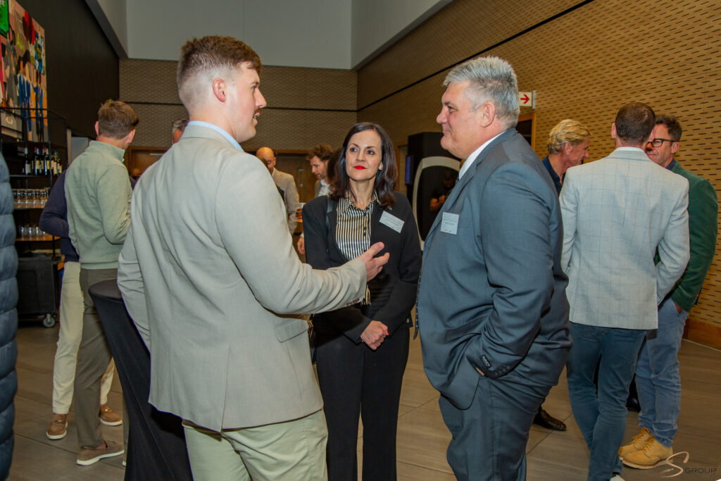 Professionals in suits chat at a networking event in a modern venue with wooden panel walls.