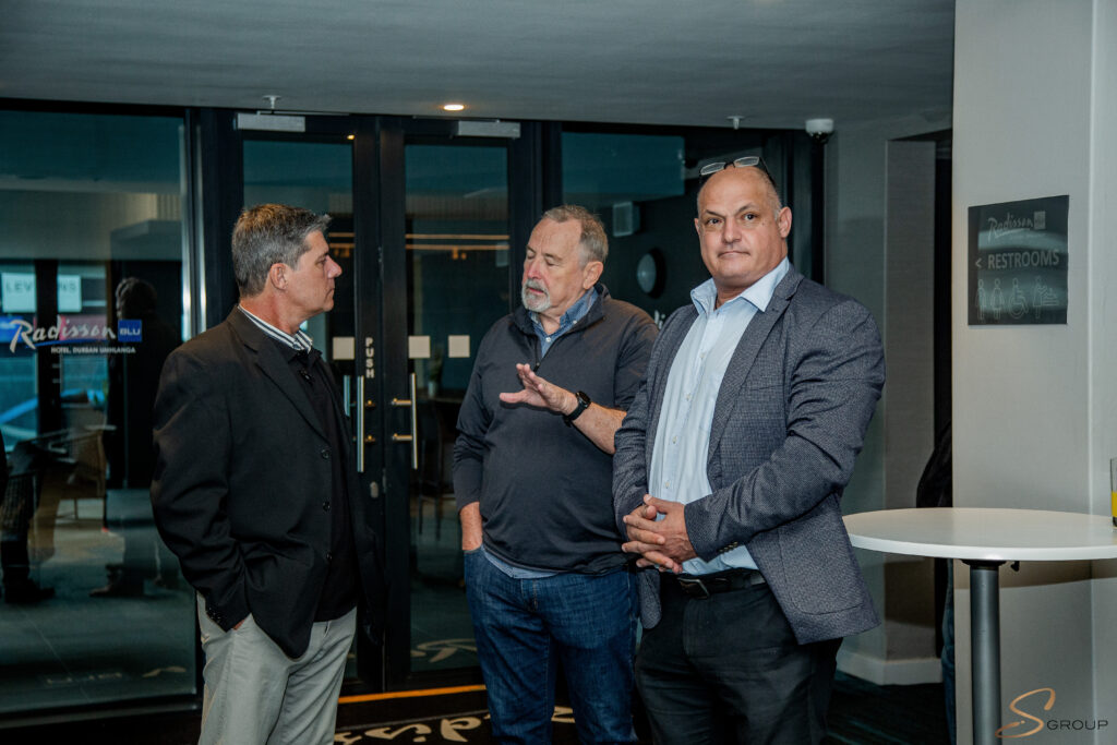 Three men in business attire conversing in a modern lobby near glass doors.