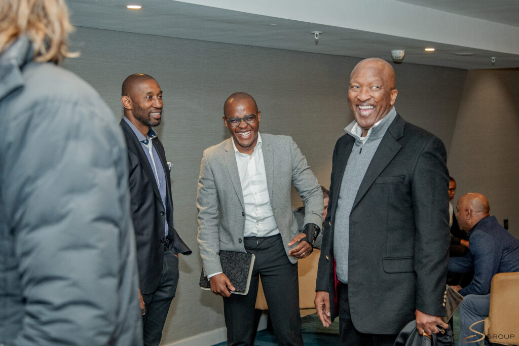 Group of professionals in suits smiling and laughing in a hallway during a meeting.