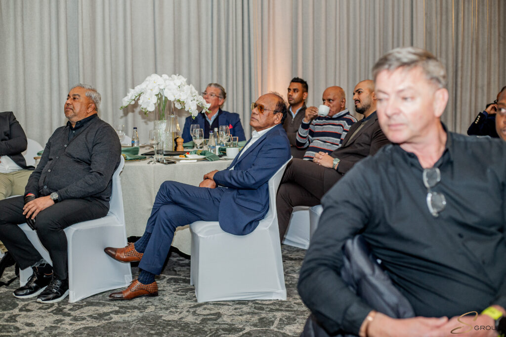 Group of men seated around a round table at a formal event, with white orchid centerpiece and glassware in a banquet setting.